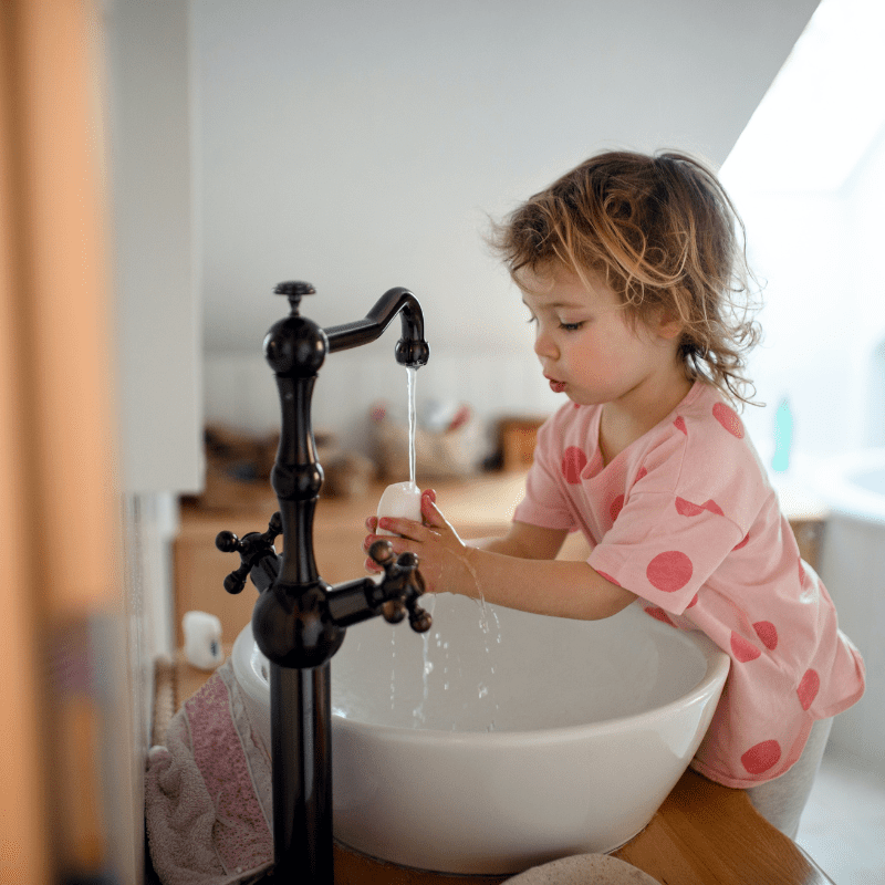 Small child playing with water and soap at bathroom