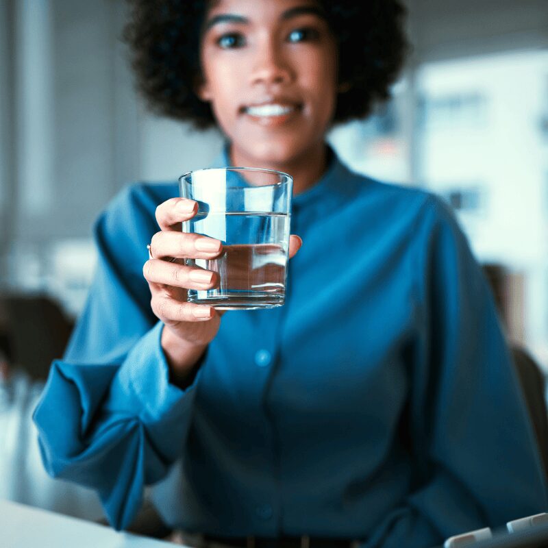 woman-glass-and-water-in-portrait-office-smiling woman holding out glass of water in office