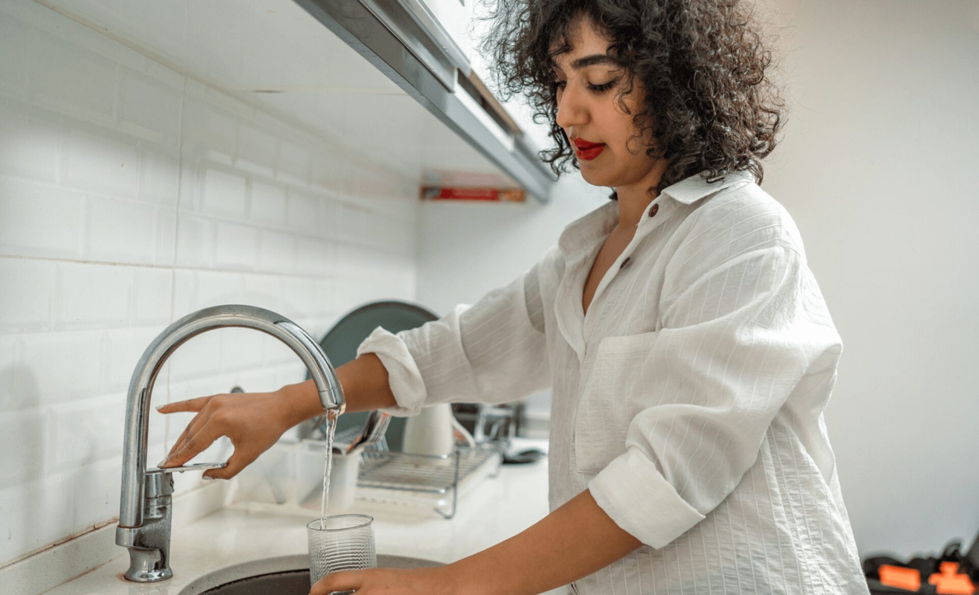 young black woman filling a glass of water at the kitchen faucet.