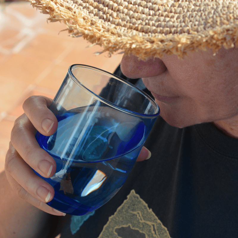 woman-drinking-a-glass-of-water-outdoors woman in straw hat drinking water out doors