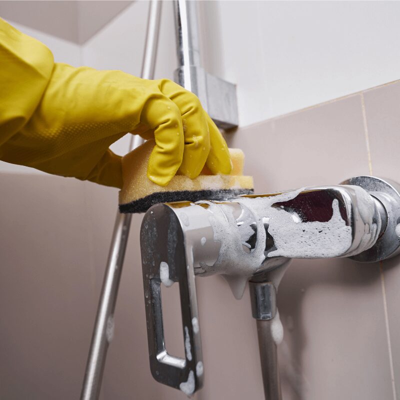 close up of someone wearing yellow rubber gloves cleaning hard water stains on shower faucet