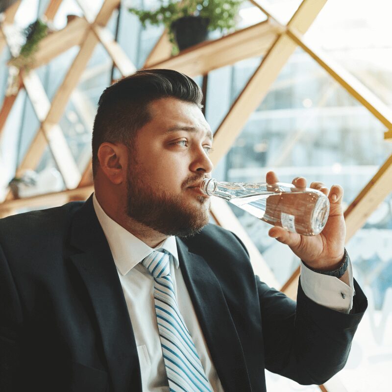 Business man in a black suit and tie, sipping water from a reusable water bottle