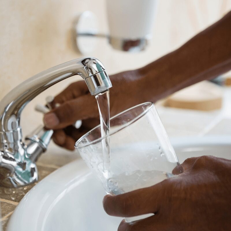 cropped hand of a man filling water glass at the sink