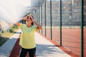 Attractive fitness lady feeling tired after morning run young woman in workout clothes, stopping to take a breather and wipe sweat from her forehead.