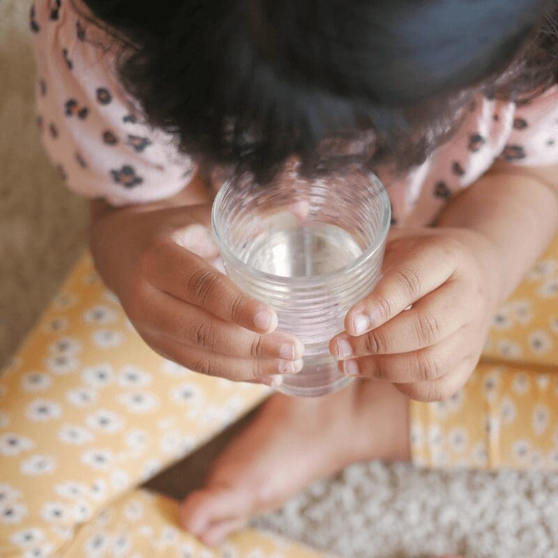 child-holds-glass-of-water-while-sitting overhead view of a child holding a glass of water
